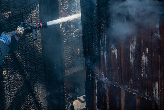 Strong brave firefighter using extinguisher and water from hose for fire fighting. Firefighter spraying high pressure water to fire. Firefighter training with dangerous flames