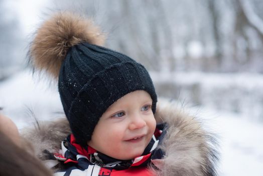 Funny laughing baby in winter outside. Cute toddler kid in a warm snowsuit and hat discovered winter forest. Snow, red cheeks, smile on face