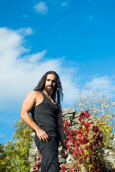 Freedom, feel good, travel and adventure concept. Stylish handsome macho man standing against sky and colorful ivy leaves. Man lifestyle. Man fashion and wellness concept