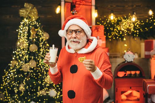 Portrait of bearded funny man in Santa costume. Santa Claus enjoys cookies and milk left out for him on Christmas eve. Milk and cookies for Santa Claus. Santa picking cookie