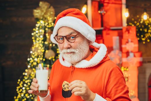 Portrait of bearded funny man in Santa costume. Santa fun. Santa Claus eating cookies and drinking milk on Christmas Eve. Christmas Beard style