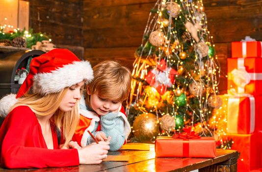 Young mother helping her son write a letter to Santa. Winter holidays and childhood concept. Xmas tree. Helper of Santa with a Christmas magic gifts. Happy holiday concept