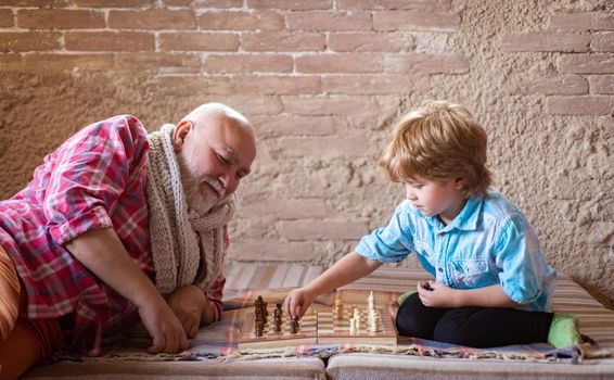 Grandfather and grandson are playing chess and smiling while spending time together at home.