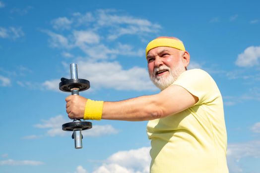 Grandfather sportsman portrait on blue sky backgrounds. Portrait of healthy senior. Senior man in his seventies training and lifting weigh
