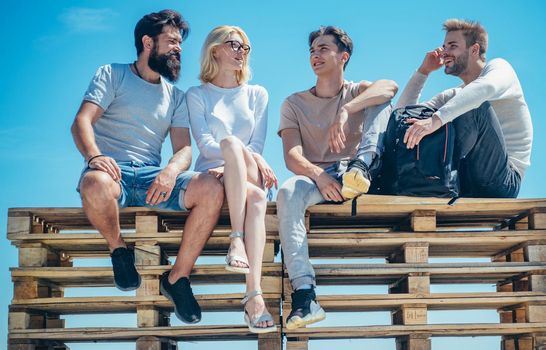 Group of friends students having break and chating together sitting at clear sky background. Friendship and studentship concept. Best friends spend their leisure time outdoor