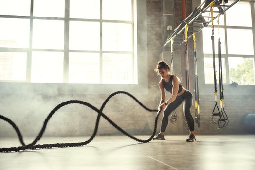 Strong and beautiful. Young athletic woman with perfect body doing crossfit exercises with a rope in the gym. CrossFit concept. Workout. Exercises concept