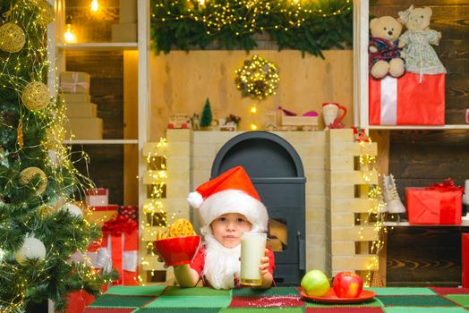 Thanksgiving day and Christmas. Happy Santa Claus - cute boy child eating a cookie and drinking glass of milk at home Christmas interior