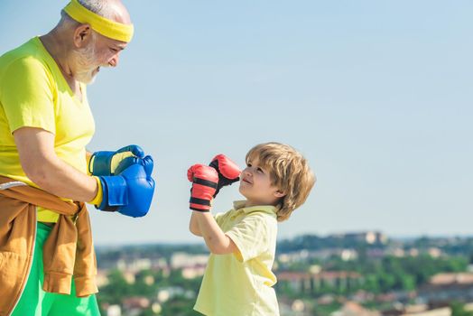 Grandpa and little child boy in boxing stance doing exercises with boxing gloves. Elderly man hitting punching bag. Grandfather and child fighting poses