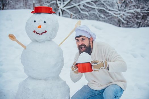 Christmas cookery. Funny Christmas cook. Happy father chef playing with a snowman on a snowy winter walk. Santa Claus cook wishes Merry Christmas