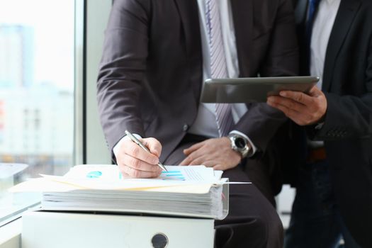 Two businessman are looking and studying statistics on tablet display closeup. Male hand opponent holds pen and points out problem collaboration business coach cooperation partnership palm concept