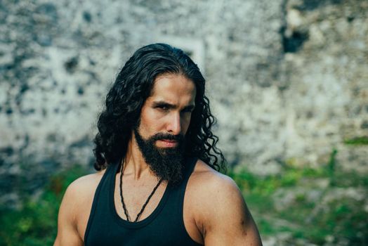 Young stylish man with determined character. Strong confident man with long wavy dark hair and beard looking at camera. Mans power and confidence concept