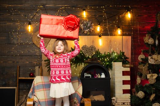 The concept of giving and receiving gifts. Cheerful smiling happy little cute girl holding gigantic gift present from Santa. Christmas eve and magic concept. Bright New Years interior