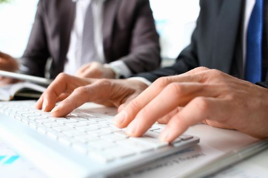 Male arms in suit typing on white keyboard using computer pc at office workplace closeup. Accountant finger job modern lifestyle web search assistant enter account login password and note teamwork