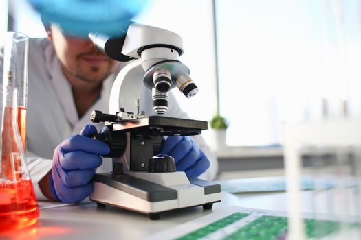 Portrait of a young chemist looking in binocular microscope looking for pathology analyzes patient at medical hospital for treatment disease tumors