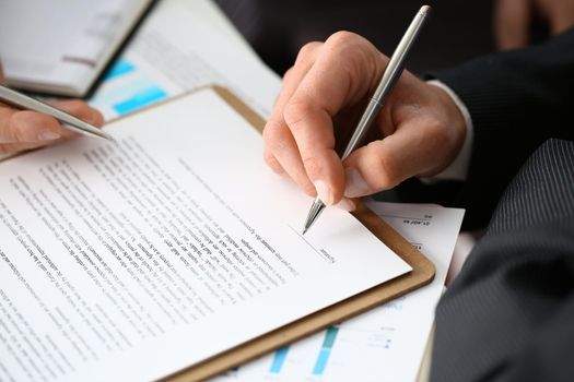 Male arm in suit and tie fill form clipped pad with silver pen closeup. Sign gesture read pact sale agent bank job make note loan credit mortgage investment finance executive chief legal teamwork law