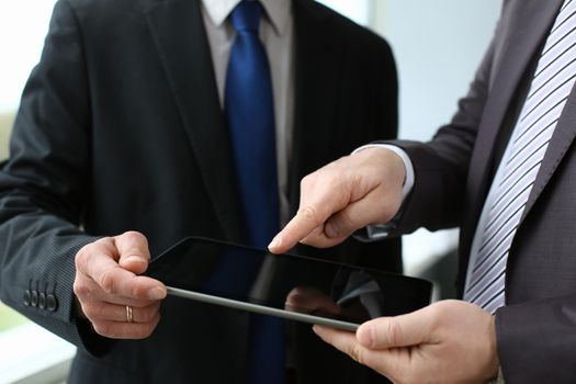 Two businessman are looking and studying statistics on tablet display closeup. Male hand opponent holds pen and points out problem collaboration business coach cooperation partnership palm concept