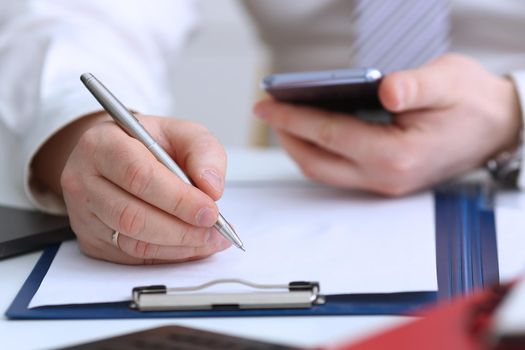 Male arm in suit and tie hold silver pen filling schedule in notepad at office workplace closeup. Legal law consult assistance gesture or finance investment advisor clerk job information gesture