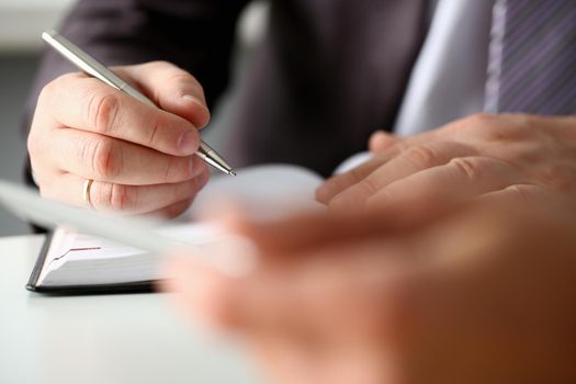 Hand of businessman in suit filling and signing with silver pen partnership agreement form clipped to pad closeup. Management training course some important document, team leader ambition concept