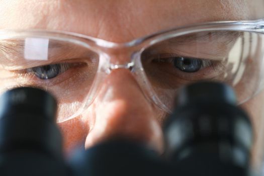 Handsome man scientist looking through binocular microscope examining diseases of the virus that infects water vivo ivf