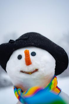 Funny snowman in stylish hat and scarf on snowy field. Snowman gentleman in winter hat. Cute little snowman outdoor. Christmas snowman close up with scarf.