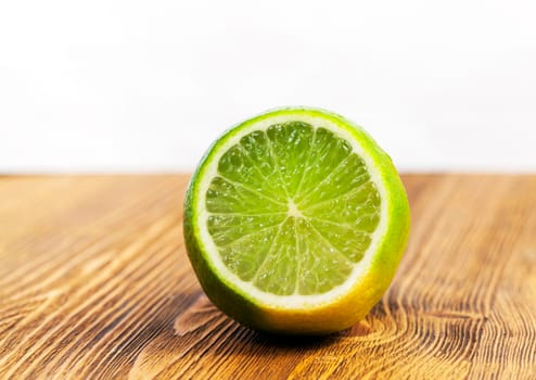 a cut piece of sour green lime lying on a brown wooden table. Photo close-up. Focus on fruit