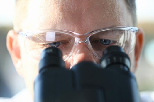 Handsome man scientist looking through binocular microscope examining diseases of the virus that infects water vivo ivf
