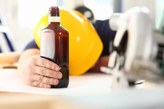 Arm of drunken worker in yellow helmet hold liquor bottle portrait. Manual job workplace DIY inspiration fix shop hard hat industrial education profession career