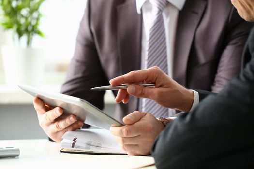 Two businessman are looking and studying statistics on tablet display closeup. Male hand opponent holds pen and points out problem collaboration business coach cooperation partnership palm concept