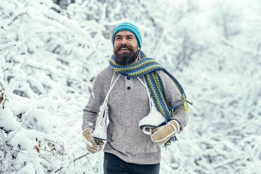 Man with skates in snowy forest. Man in thermal jacket, beard warm in winter. Winter sport and rest, Christmas. Bearded handsome man, Santa Claus.