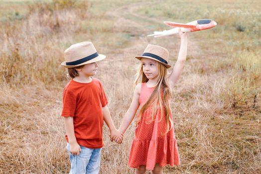 Little children - daughter and son is playing and dreaming of flying. Child care. Cute children - daughter and son playing with toy airplane in the meadow in vintage color tone