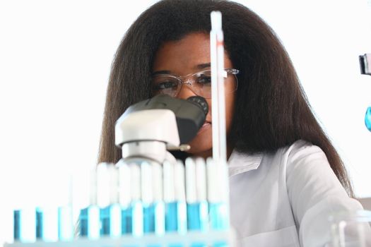 Black woman scientist student chemist in protective goggles are conducting research using microscope for bacterial contamination of water to search for vaccine to treat diseases in medicine.