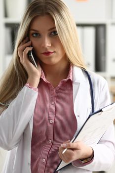Beautiful female blond doctor talking on phone at the office woman discussing the disease and giving online consultation remote training education