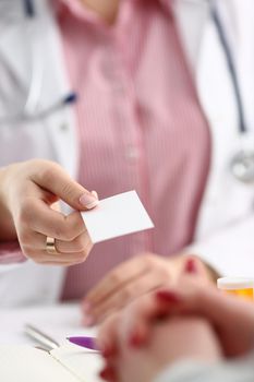 Female physician hand give white blank calling card to businesswoman closeup in office. Physical disease prevention examine patient instrument shop healthy lifestyle family doctor concept