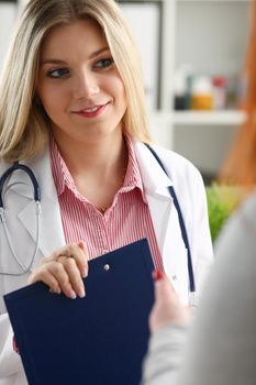Smiling beautiful female medicine doctor explain diagnosis to male patient in business suit holding and showing pad. Physical disease prevention 911 prescribe remedy healthy lifestyle concept