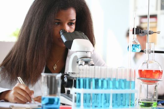 Black woman scientist student chemist in protective goggles are conducting research using microscope for bacterial contamination of water to search for vaccine to treat diseases in medicine.