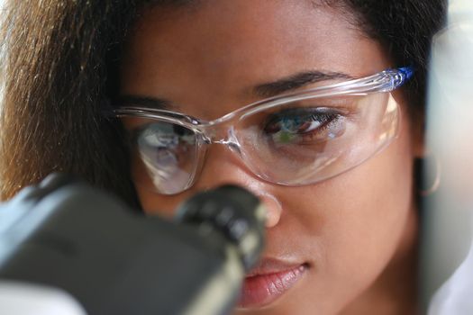 Black woman scientist student chemist in protective goggles are conducting research using microscope for bacterial contamination of water to search for vaccine to treat diseases in medicine.