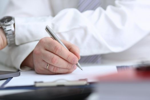 Male arm in suit and tie hold silver pen filling schedule in notepad at office workplace closeup. Legal law consult assistance gesture or finance investment advisor clerk job information gesture