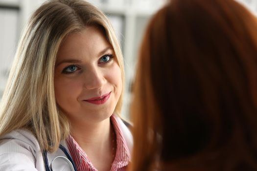 Handsome friendly female doctor talk with thankful female patient at office and greet her with hand on shoulder gesture. Welcoming friend trust physical healthy lifestyle exam interview concept