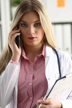 Beautiful female blond doctor talking on phone at the office woman discussing the disease and giving online consultation remote training education