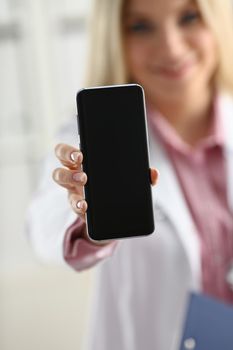 Beautiful female blonde doctor holding smartphone in hand at office woman discussing disease and giving an online consultation to a remote training mobile advertising app