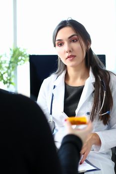 Female medicine doctor hand hold jar of pills and write prescription to patient at worktable. Panacea and life save prescribing treatment legal drug store concept.