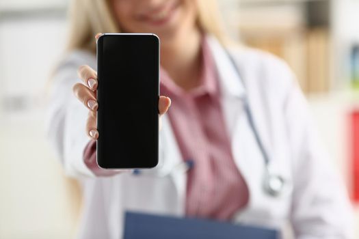 Beautiful female blonde doctor holding smartphone in hand at office woman discussing disease and giving an online consultation to a remote training mobile advertising app