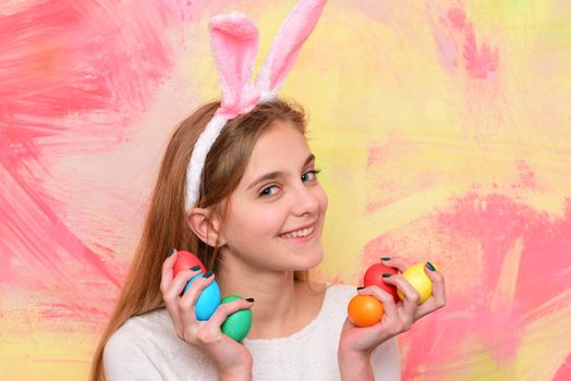 Happy smiling little teen girl with bunny ears holding painted easter eggs. Happy easter holidays concept. Cute girl celebrating easter. Cheerful kid with traditional decorations