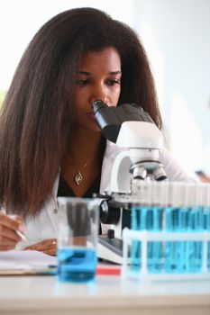 Black woman scientist student chemist in protective goggles are conducting research using microscope for bacterial contamination of water to search for vaccine to treat diseases in medicine.