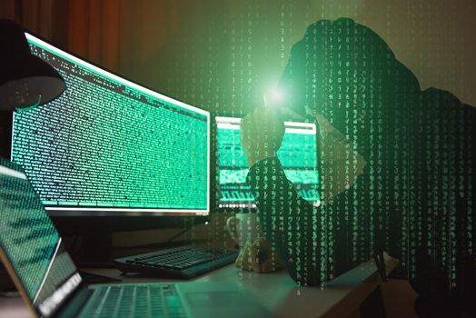 Cyber crime. Side view of young hacker in black hoodie using multiple computers and his smartphone for stealing data while sitting in dark room. Binary code. Cyber attack. Cyber security