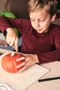 Halloween, decoration and holidays ideas- close up of kid with knife carving pumpkin or jack-o-lantern. 6 years boy has homefamily fun activity. Mom spending time with son together.