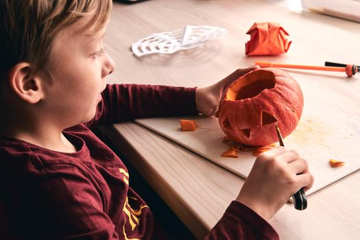 Halloween, decoration and holidays ideas- close up of kid with knife carving pumpkin or jack-o-lantern. 6 years boy has homefamily fun activity. Mom spending time with son together.