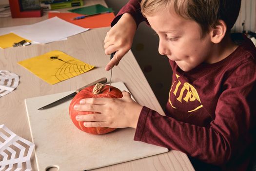 Halloween, decoration and holidays ideas- close up of kid with knife carving pumpkin or jack-o-lantern. 6 years boy has homefamily fun activity. Mom spending time with son together.