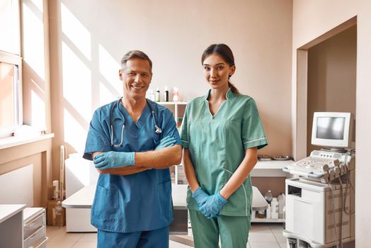 Professional team. Two positive vets in work uniform are smiling and looking at camera while standing at the veterinary clinic. Pet care concept. Medicine concept. Animal hospital