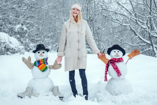 Winter woman. Funny Girl Love winter. Winter portrait of young woman in the winter snowy scenery. Cute girl making snowman on snowy field outdoor
